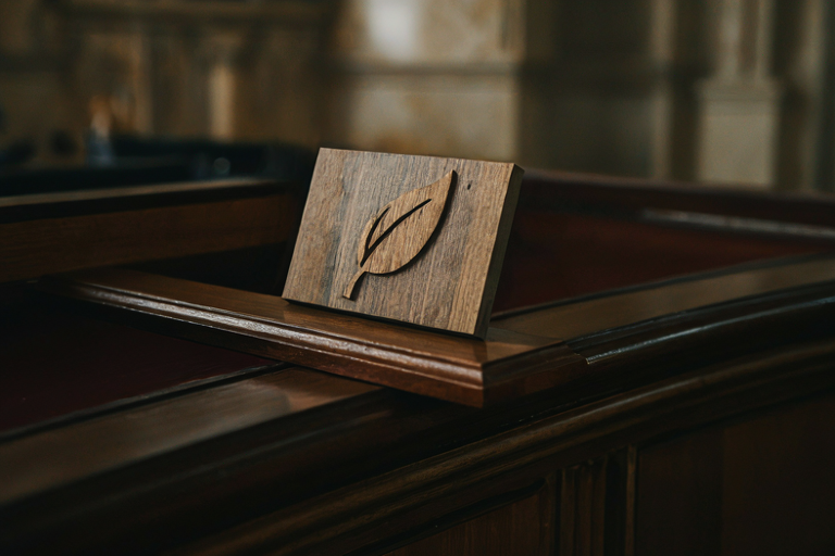 Editorial illustration of a stylized wooden sign representing a national slogan, set on a dark polished surface under focused light in a formal, blurred setting.