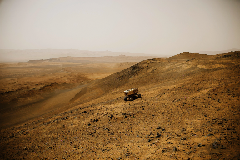 A robotic rover situated on the dusty, rocky terrain of Mars, overlooking a vast Martian ridge.