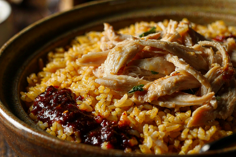 A close-up editorial illustration of com ga, featuring golden turmeric rice topped with shredded chicken and a side of red chili jam.