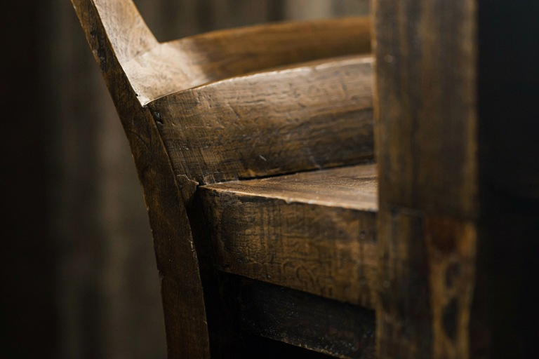 A solitary, dark wooden chair under a focused beam of light in a shadowed, contemplative setting.