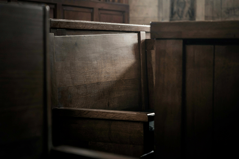 A solitary, dark wooden chair in a dimly lit, formal courtroom setting, emphasizing judgment and gravity.
