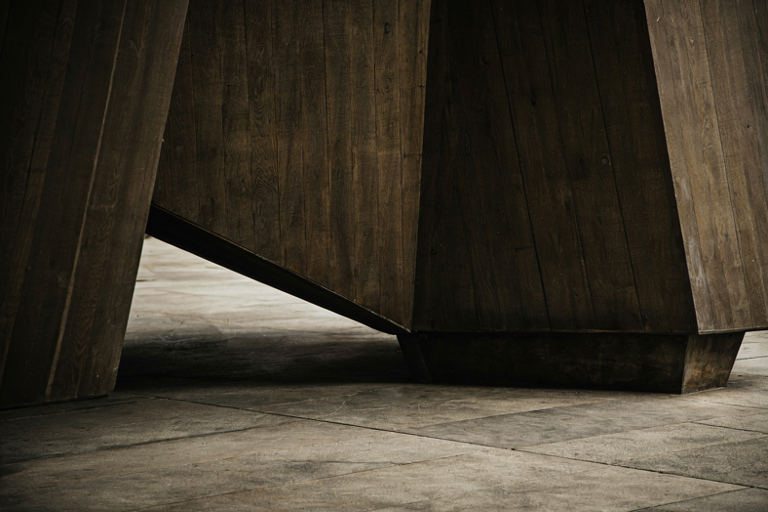A stark, monumental interior featuring a heavy, dark wooden firing squad block on a cold stone floor, illuminated by dramatic, high-contrast lighting.