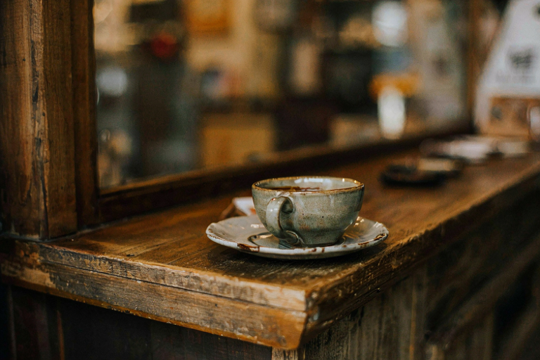 A close-up illustration of a handcrafted ceramic coffee mug and saucer resting on a worn wooden counter in a cozy, independent cafe, emphasizing local character.