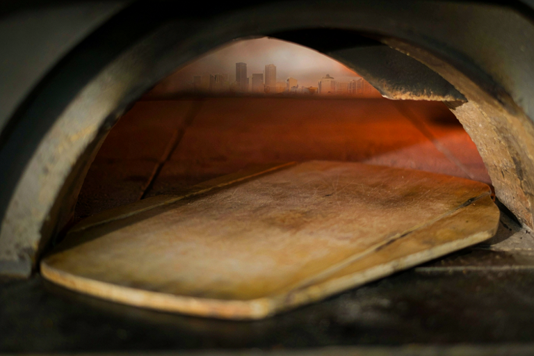 Wooden pizza peel and stone oven with blurred city skyline