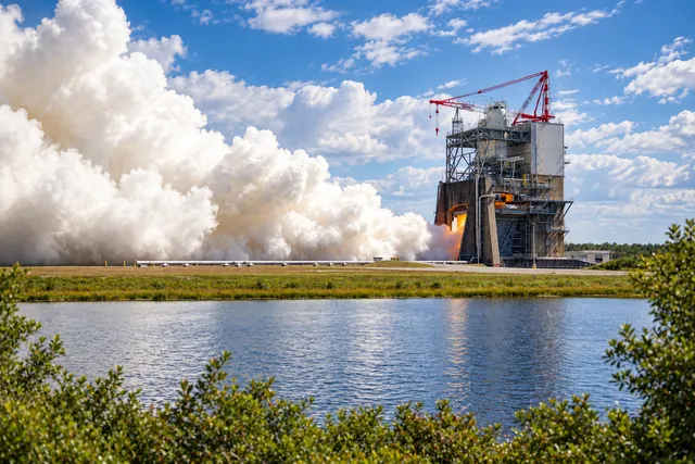 AI illustration based on reference photographs; not an event photograph. Industrial rocket engine test stand with a red crane and a plume of white smoke against a partly cloudy sky.