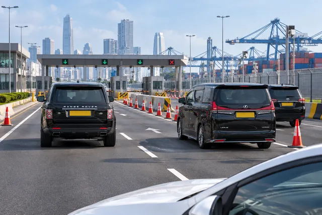 AI illustration based on reference photographs; not an event photograph. Editorial illustration of a modern urban road leading to a port entrance, emphasizing traffic management infrastructure with a black SUV in the scene.