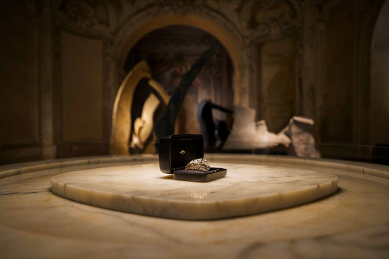 A black case with a minimalist dial displays a delicate high jewellery piece, illuminated by warm light.