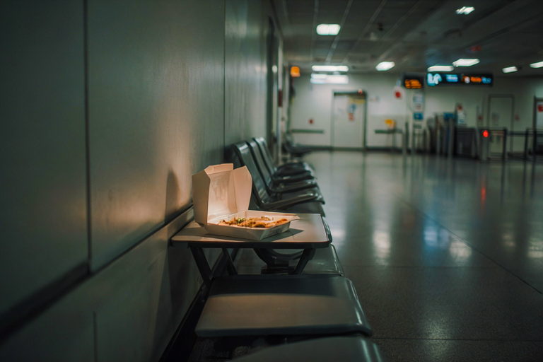 A plain meal box sits on a table in a dimly lit airport waiting area, illuminated by soft light.