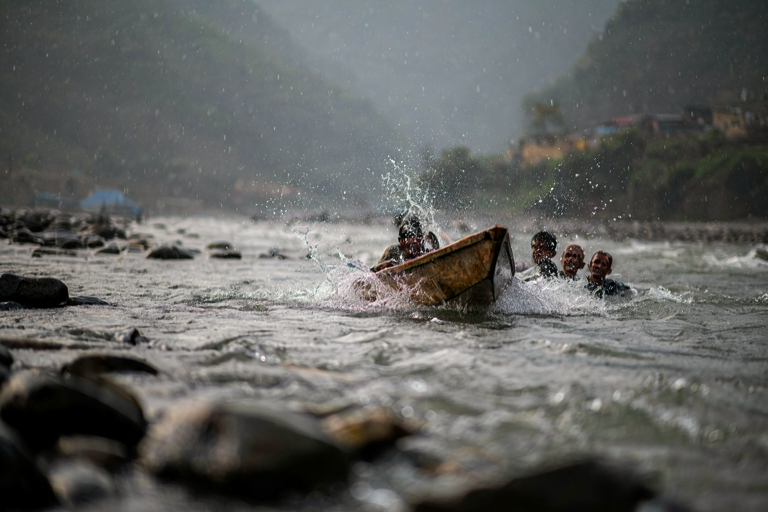 A realistic illustration of flood victims in Nepal, showing people struggling in floodwaters and a simple wooden boat in the center of the frame.