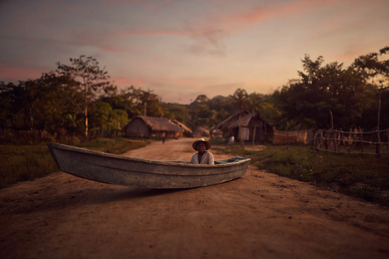 A young local guide in a wooden boat at a Guyanese village sunset, with blurred village in the background.