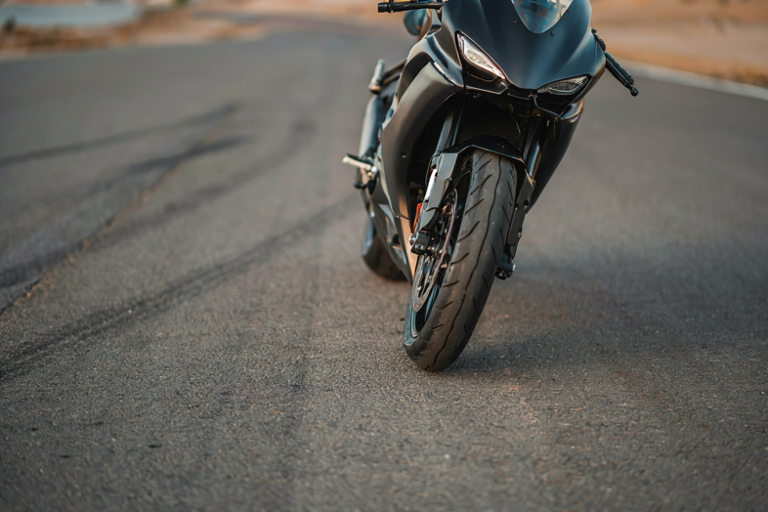 A dark racing motorcycle with a tilted front wheel on a blurred track, illuminated by directional lighting.