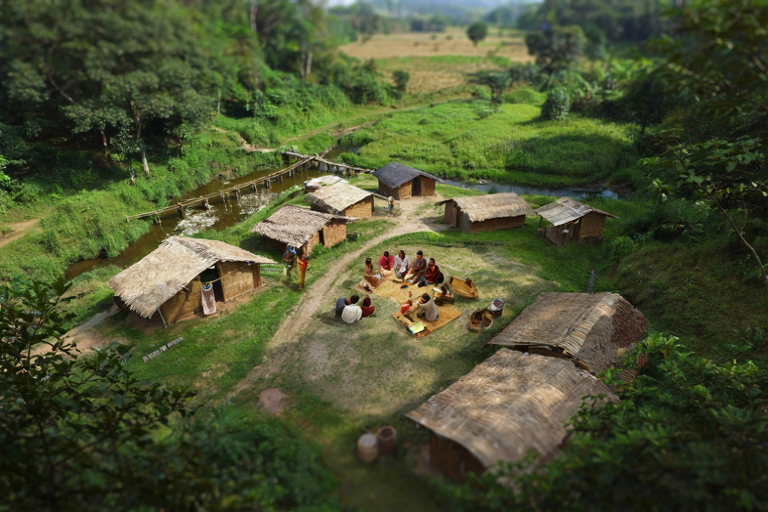 A village community gathers to discuss development plans with a small irrigation system in the background.