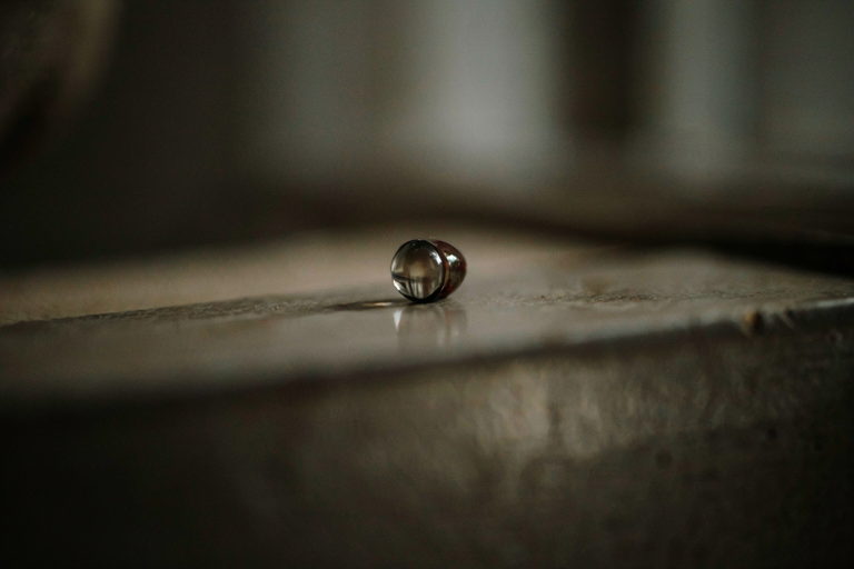 A close-up illustration of a small, dark, lens-like object suggesting a pinhole camera, set against a dimly lit, textured surface.