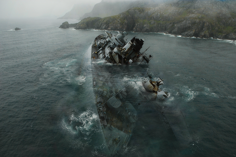 A conceptual illustration of a large, decommissioned warship sinking in the turbulent North Atlantic near a rocky coast.